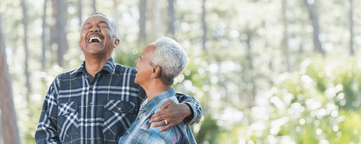 African senior couple holding hands and smiling in woods.