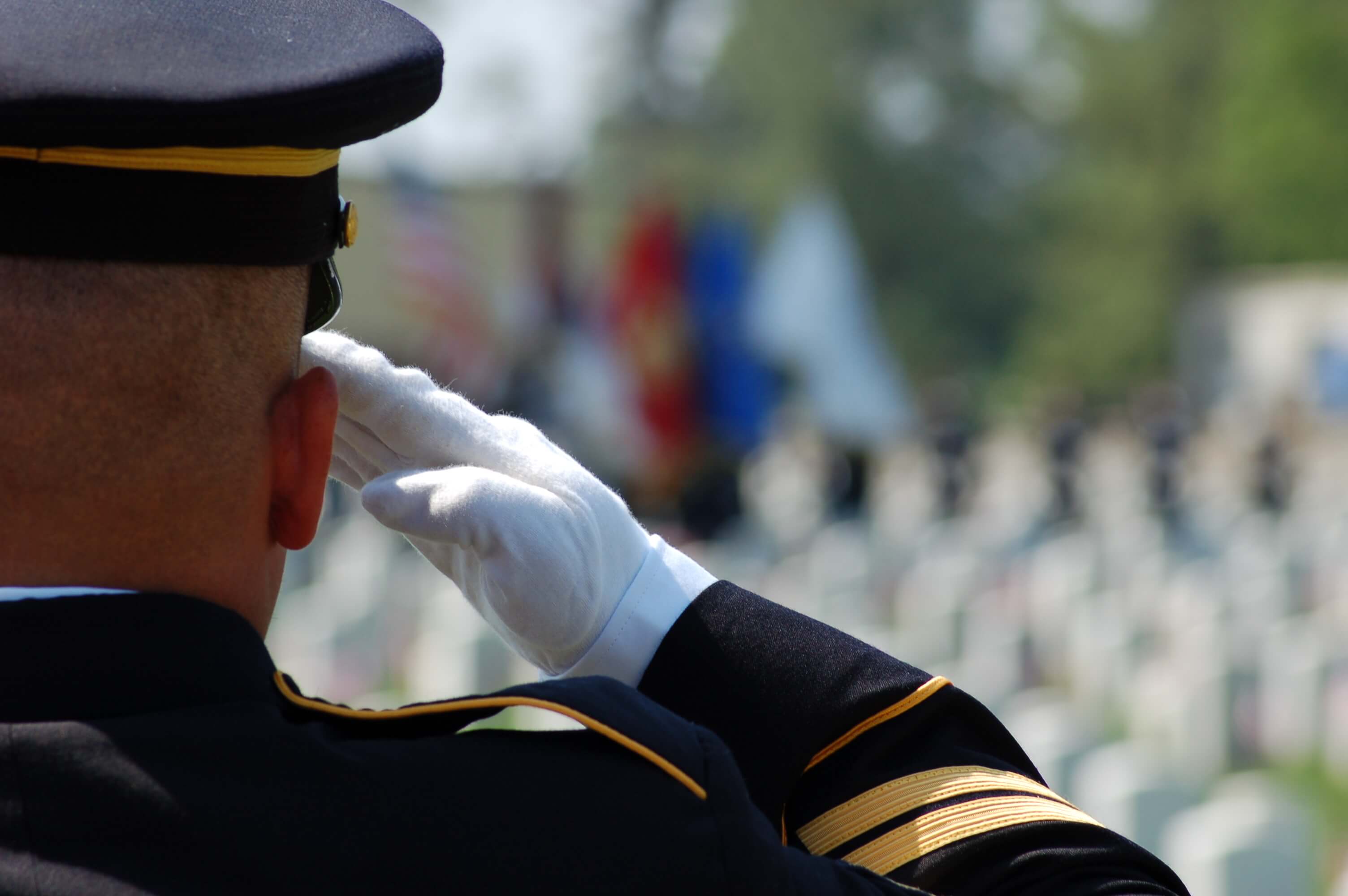 Uniformed service member wearing white gloves salutes during a military ceremony.